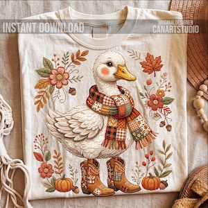 May include: Cream-colored t-shirt featuring a cartoon duck wearing a plaid scarf and cowboy boots. The duck is surrounded by fall-themed floral and leaf designs, pumpkins, and acorns. Text on the shirt reads "INSTANT DOWNLOAD" and "ORIGINAL DESIGNER CANARTSTUDIO".