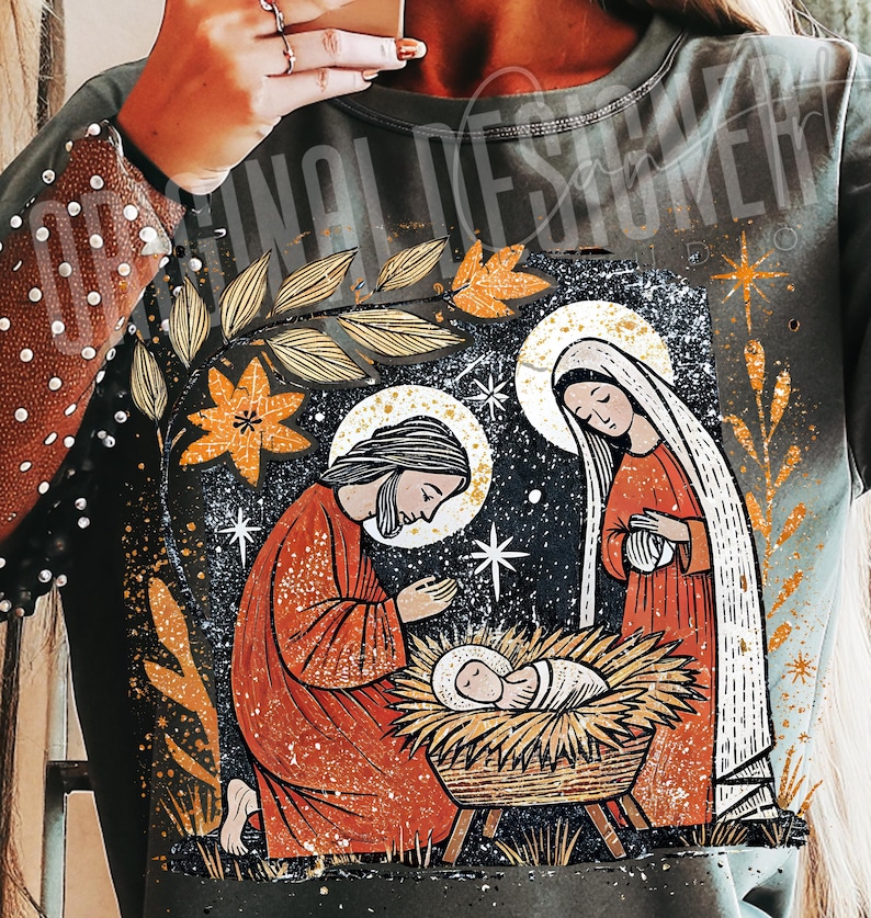 May include: A dark green long-sleeve shirt featuring a religious illustration of the Nativity scene. The design includes Joseph, Mary, and baby Jesus in a manger, with a starry night background and gold accents.