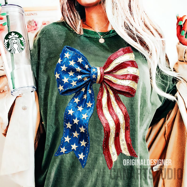 May include: A green t-shirt with a large bow design in the colours of the American flag. The bow has blue sections with gold stars and red and white striped sections. The text "ORIGINAL DESIGNER CAN ARTS STUDIO" is printed at the bottom.