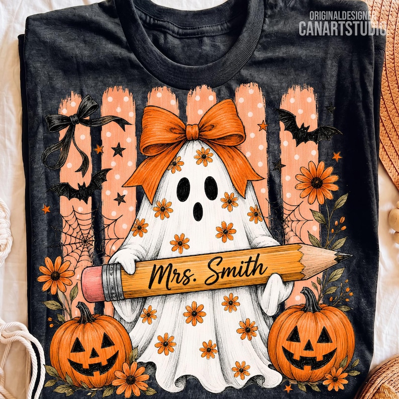 Puede incluir: Una camiseta gris oscuro con una ilustraci&oacute;n de un fantasma blanco con un lazo naranja, sosteniendo un l&aacute;piz amarillo grande con la etiqueta "Mrs. Smith". El dise&ntilde;o incluye calabazas naranjas, murci&eacute;lagos negros, telara&ntilde;as y flores.