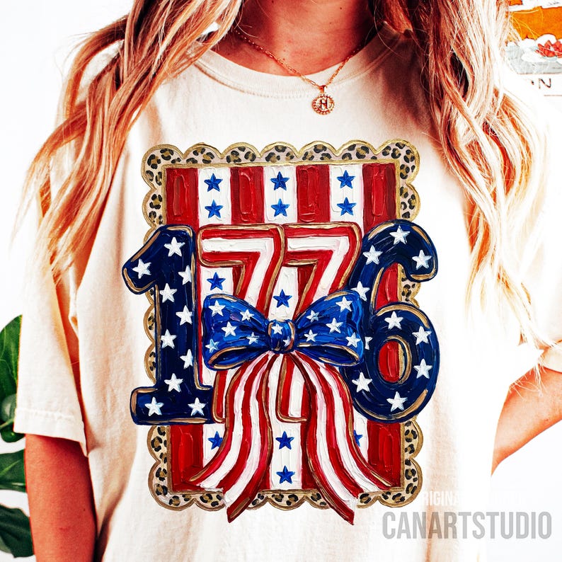 May include: Cream-colored t-shirt featuring a patriotic design with the number "1776" in blue and white, adorned with stars and stripes. A blue bow with white stars is centered on the design. The design is framed with a leopard print border.