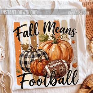 May include: White t-shirt featuring a fall-themed design. The design includes pumpkins, a football with a leopard print, and the text "Fall Means Football". The pumpkins are orange and one is black and white checkered.