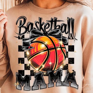 May include: A tan sweatshirt with the text "Basketball Mama" in black and white lettering. A basketball with a black bow is in the centre of the design.