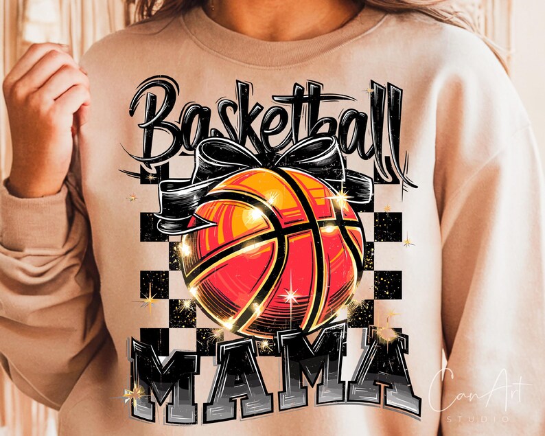 May include: A tan sweatshirt with the text "Basketball Mama" in black and white lettering. A basketball with a black bow is in the centre of the design.