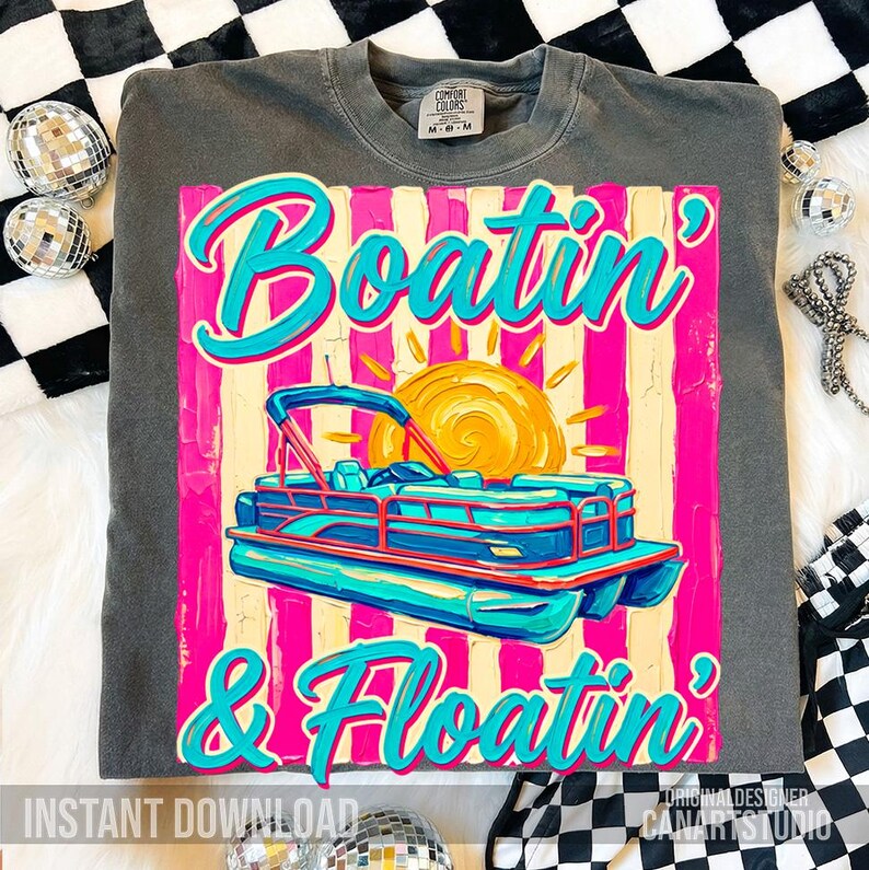 May include: Dark gray sweatshirt with a colorful graphic. The graphic features a pontoon boat, a sun, and the words "Boatin' & Floatin'" in turquoise script. The design is set against a pink and yellow striped background.