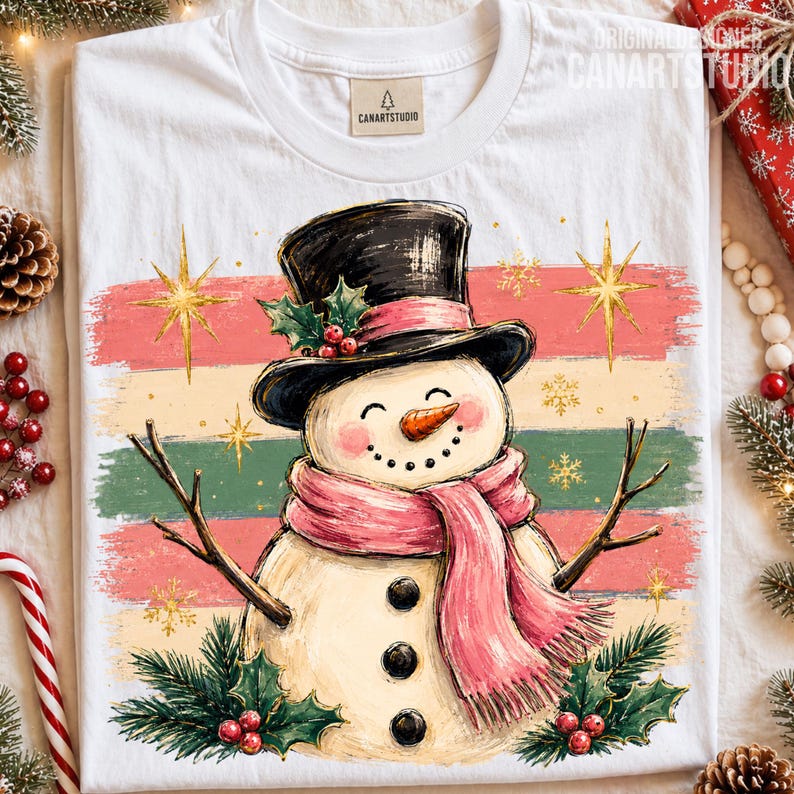 Może przedstawiać: Biały t-shirt z grafiką bałwana w czarnym cylindrze i r&oacute;żowym szaliku. Bałwan ma ramiona z gałązek, marchewkowy nos i trzy czarne guziki na tle poziomych pas&oacute;w w kolorach r&oacute;żowym, kremowym i zielonym.