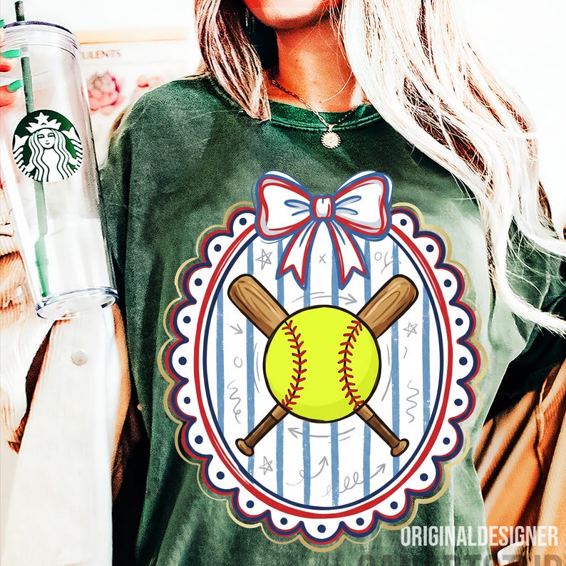 May include: Green t-shirt featuring a softball design. The design includes a yellow softball, crossed brown bats, and a red, white, and blue bow. The design is within a scalloped oval frame. The text "ORIGINAL DESIGNER" is at the bottom.