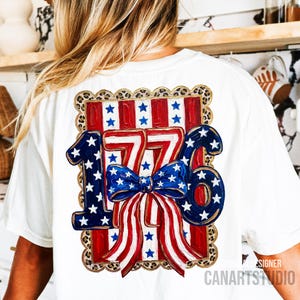 May include: White t-shirt featuring a patriotic design with the number "1776" in red, white, and blue. The design includes stars, stripes, and a bow, all within a leopard print border. The shirt is a comfortable fit.