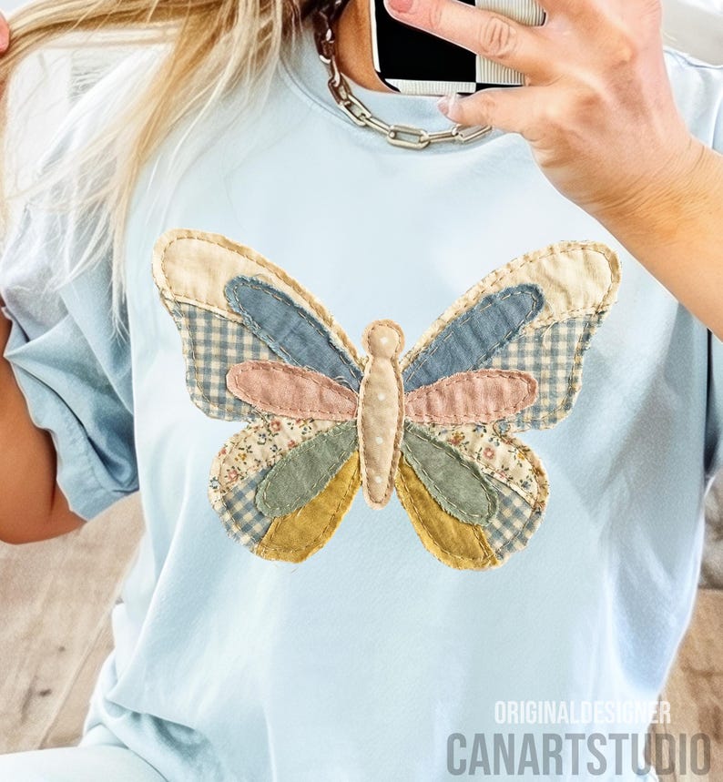 May include: Light blue t-shirt featuring a patchwork butterfly design. The butterfly has wings in various patterns and colors, including gingham, floral, and solid fabrics. The text "ORIGINAL DESIGNER CANARTSTUDIO" is visible at the bottom.