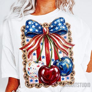 May include: White t-shirt featuring a patriotic design with a blue bow adorned with white stars, red and white striped ribbons, and three cherries. The cherries are painted in red, blue, and white with gold accents. The design is framed with a leopard print border.