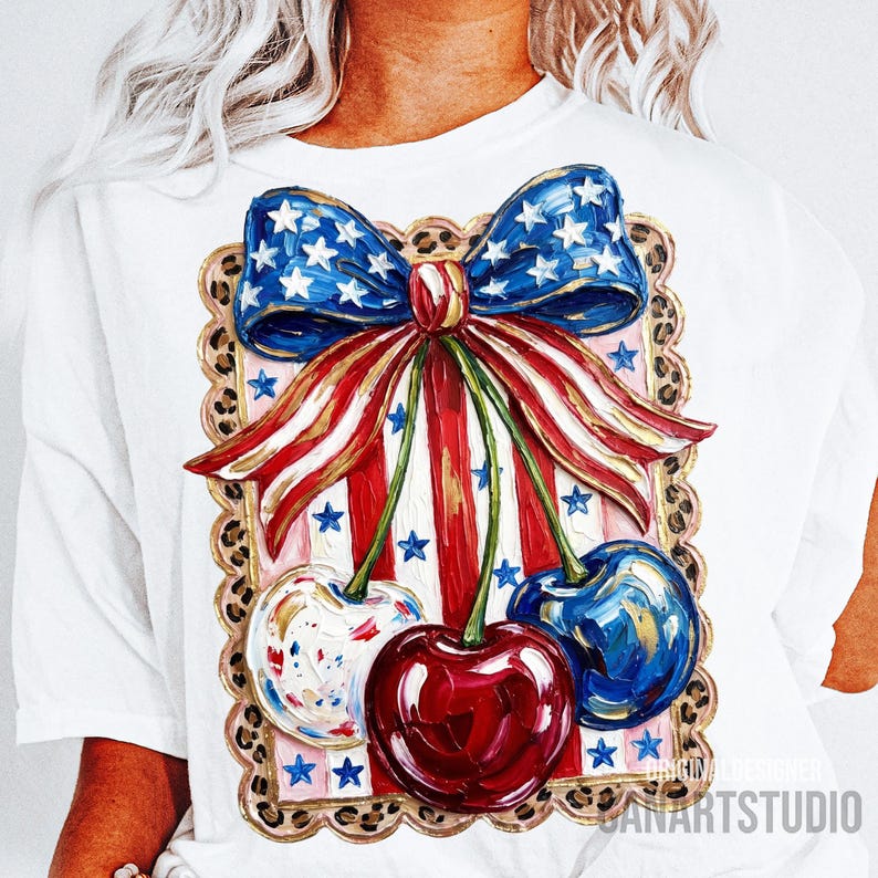 May include: White t-shirt featuring a patriotic design with a blue bow adorned with white stars, red and white striped ribbons, and three cherries. The cherries are painted in red, blue, and white with gold accents. The design is framed with a leopard print border.