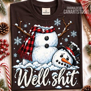 May include: A dark brown t-shirt featuring a graphic of two snowmen, one wearing a red and black plaid scarf and the other wearing a black top hat with a red band. The text "Well, shit" is printed in white script below the snowmen among snowflakes.