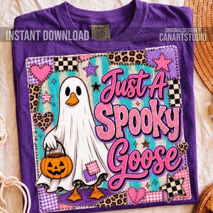 Op de afbeelding: Een paars t-shirt met een afbeelding van een witte gans verkleed als spook, die een oranje pompoenemmer vasthoudt. Het ontwerp bevat de tekst Just A Spooky Goose in het roze, omringd door patchworkpatronen van hartjes, sterren en ruitjes.