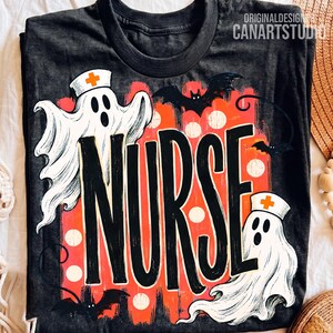 May include: A charcoal gray t-shirt featuring a graphic with the word NURSE in large black letters. The design includes two white ghosts wearing nurse caps with orange crosses, three black bats, and an orange background with white dots.