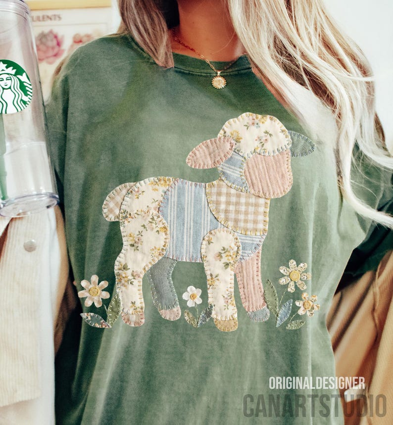 Puede incluir: Camiseta verde oliva con un dise&ntilde;o de cordero de patchwork. El cordero est&aacute; hecho de telas florales, a rayas y a cuadros. Flores bordadas rodean al cordero. El texto "ORIGINAL DESIGNER CANARTSTUDIO" est&aacute; impreso en la parte inferior derecha.
