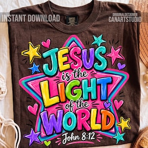 May include: A dark brown t-shirt featuring a large, colorful graphic of a star with the text "JESUS is the LIGHT of the WORLD" and "John 8:12" in vibrant, multi-colored lettering. The design includes various small stars and hearts.