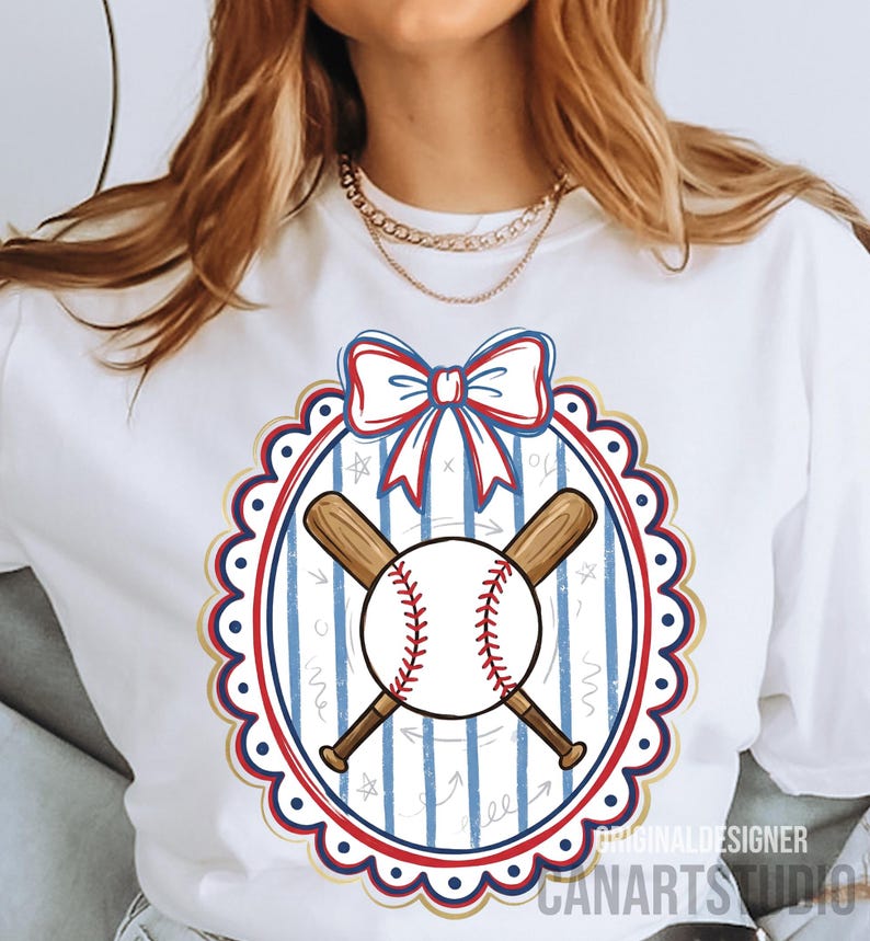 May include: White t-shirt featuring a baseball design. The design includes a baseball with red stitching, crossed wooden bats, and a bow. The design is framed by a red, white, and blue oval with a scalloped edge. The text "CANARTS STUDIO" is visible.