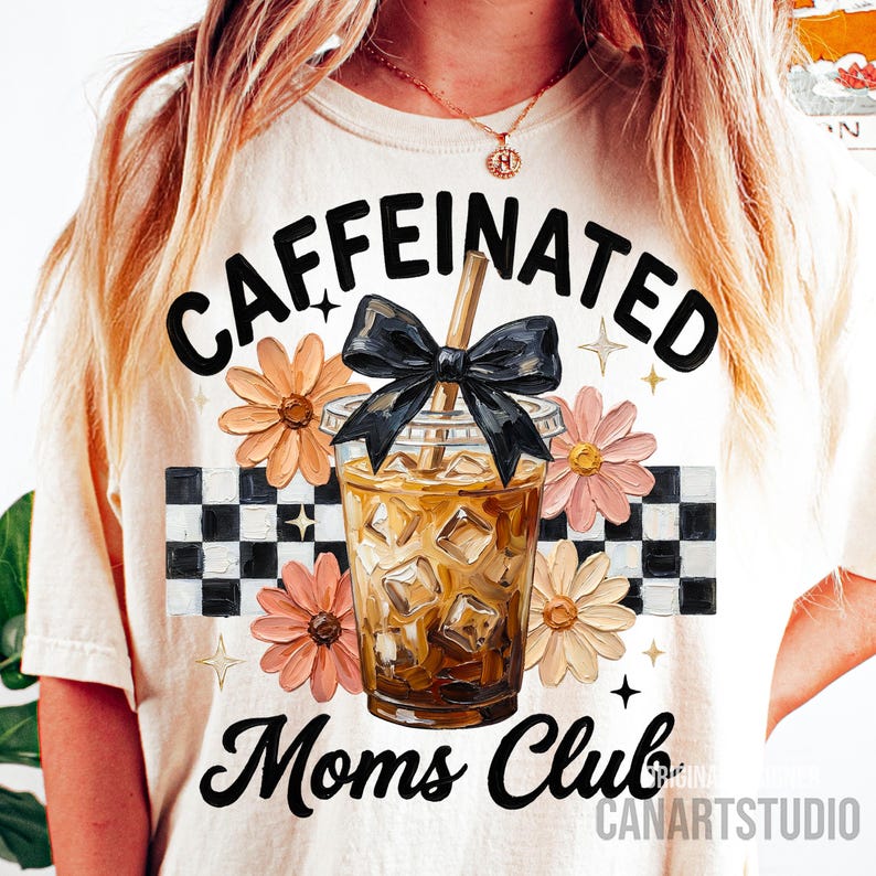 May include: Cream-colored t-shirt with the words "CAFFEINATED Moms Club" in black script. The design includes a graphic of an iced coffee drink with a black bow, surrounded by flowers and a checkered pattern.