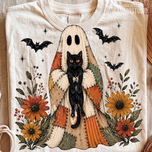 May include: A cream-colored t-shirt featuring a graphic of a black cat wearing a patchwork ghost costume. The design includes orange and yellow flowers, green leaves, and black bats flying against a background of small black stars.