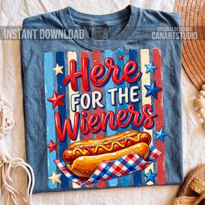May include: Blue t-shirt with a graphic of a hot dog and the text "Here for the Wieners." The design includes red, white, and blue stripes and star accents. The shirt has a crew neck and short sleeves.