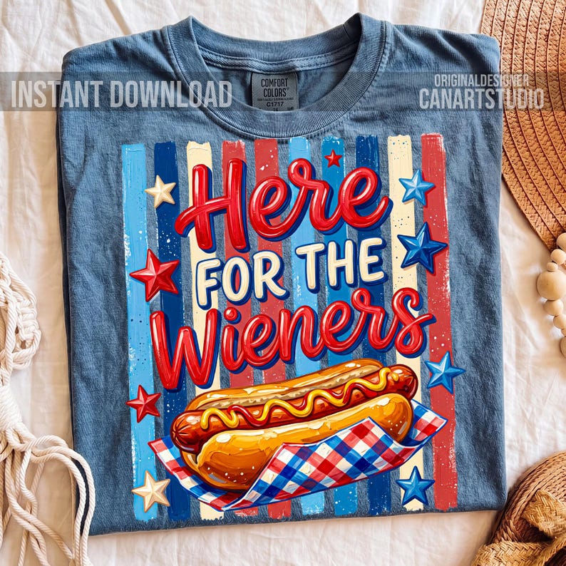 May include: Blue t-shirt with a graphic of a hot dog and the text "Here for the Wieners." The design includes red, white, and blue stripes and star accents. The shirt has a crew neck and short sleeves.