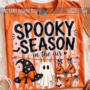 Może przedstawiać: Pomarańczowy t-shirt z grafiką i napisem SPOOKY SEASON in the air. Wzór przedstawia czarny kapelusz czarownicy z pomarańczową kokardą, białego ducha oraz pomarańczowe bikini w czarne nietoperze, zawieszone na sznurku do suszenia prania.