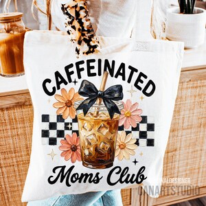 May include: White tote bag with a graphic design featuring the words "CAFFEINATED Moms Club" in black script. The design includes a coffee drink with ice cubes, flowers, and a black bow. A checkered pattern is also present.