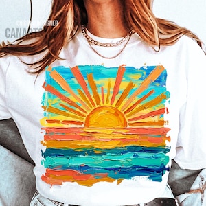 May include: White t-shirt featuring a vibrant, impressionistic painting of a sunset over the ocean. The artwork uses thick brushstrokes in shades of orange, yellow, blue, and turquoise. The text "ORIGINAL DESIGNER CANARTS" is visible.