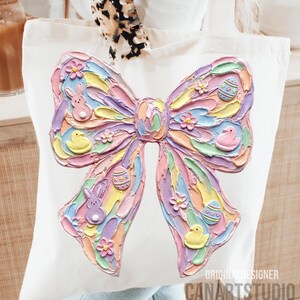 May include: White tote bag featuring a large, textured bow design in pastel colors. The bow is decorated with Easter-themed elements like eggs, flowers, bunnies, and chicks. The words "ORIGINAL DESIGNER" and "CANARTSTUDIO" are printed on the bottom right.