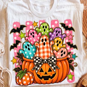 May include: A white t-shirt featuring a graphic of a large orange jack-o'-lantern filled with colorful ghosts in polka dot and gingham patterns. The design includes black bats, yellow and green stars, and a black and white checkered bow on the pumpkin.