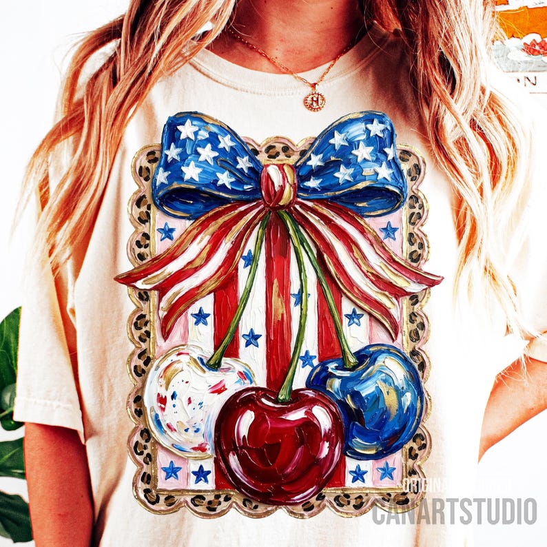 May include: Cream-colored t-shirt featuring a patriotic design. The graphic includes a blue bow with white stars, red and white stripes, and three cherries in red, white, and blue. The design is framed with a leopard print border.