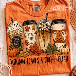 May include: An orange t-shirt featuring a graphic of four coffee cups decorated with ghosts, pumpkins, and autumn leaves. The text reads "Sippin' on magic", "Hello, fall!", and "Autumn leaves & coffee please". The shirt has a Comfort Colors label.
