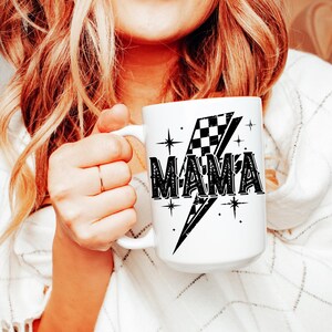 May include: White ceramic mug with a black and white checkered flag design and the word "MAMA" in a bold, black font. The flag is on a lightning bolt shape with stars around it.