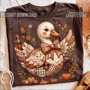 May include: Brown t-shirt featuring a whimsical duck design with patchwork wings and a bow. The duck has a white body, orange beak and feet, and is surrounded by pumpkins and floral accents. The text "INSTANT DOWNLOAD" and "CANARTSTUDIO" are visible.