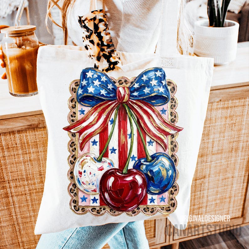 May include: White canvas tote bag featuring a patriotic design. The design includes a blue bow with white stars, red and white striped ribbons, and three cherries. The cherries are painted in red, blue, and white with star accents. The bag has a leopard print handle.
