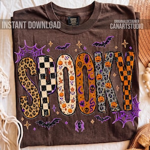 May include: Brown t-shirt with the word "SPOOKY" in a variety of patterns and colors. The letters feature leopard print, checkerboard, floral, and pumpkin designs. Bats, spiderwebs, and stars surround the word, creating a festive Halloween theme.