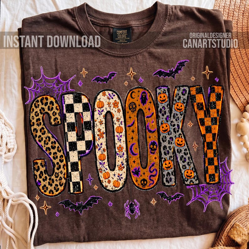 May include: Brown t-shirt with the word "SPOOKY" in a variety of patterns and colors. The letters feature leopard print, checkerboard, floral, and pumpkin designs. Bats, spiderwebs, and stars surround the word, creating a festive Halloween theme.