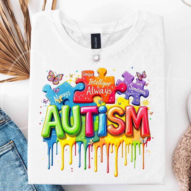 May include: White t-shirt with a colorful graphic design of puzzle pieces spelling out "AUTISM". The puzzle pieces have text on them that reads "Unique", "Intelligent & Always", "Really Sometimes Mysterious".