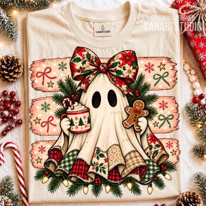 May include: A cream-colored t-shirt featuring a graphic of a ghost wearing a large poinsettia-patterned bow, holding a mug with a candy cane and a gingerbread cookie. The design includes pine branches, red berries, and string lights.