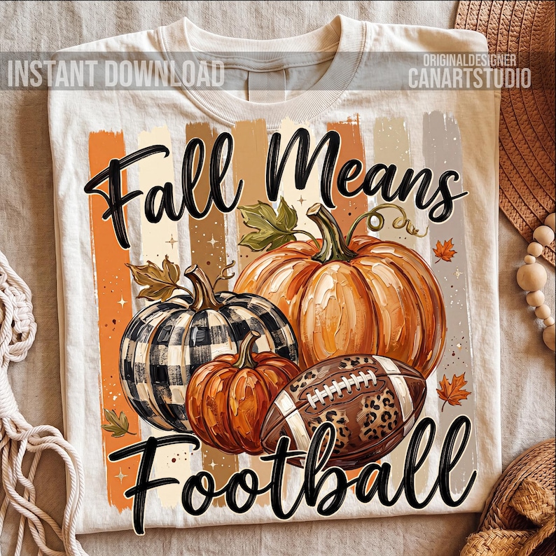 May include: Cream-colored t-shirt with a fall-themed graphic. The design features pumpkins, a football with a leopard print, and the text "Fall Means Football". The design includes orange, brown, and black colors.