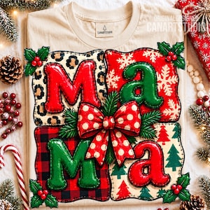 May include: A beige t-shirt featuring a graphic of the word MAMA in a four-paneled quilt design. Each letter is puffy and stitched, set against backgrounds of leopard print, white snowflakes on red, red plaid, and green trees on cream.