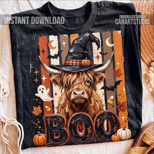 Puede incluir: Camiseta negra con un diseño de Halloween. El diseño presenta una vaca de las Tierras Altas con un sombrero de bruja, con la palabra "BOO". Incluye calabazas, murciélagos y hojas de otoño.