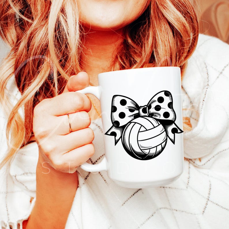 May include: White ceramic mug with a black and white illustration of a volleyball with a polka dot bow.