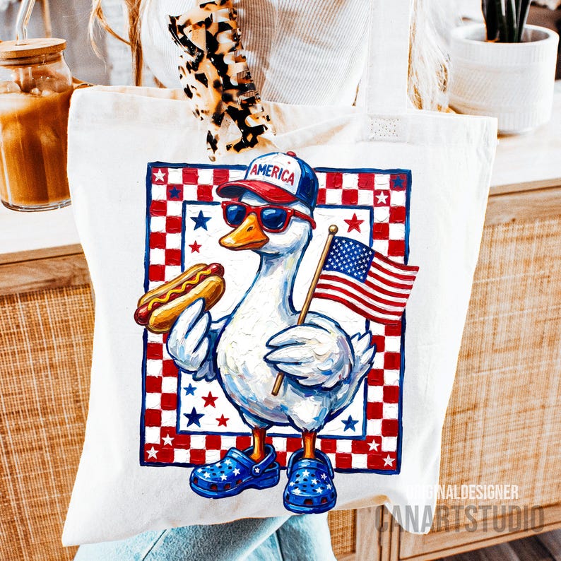 May include: White tote bag featuring a patriotic goose wearing sunglasses, a baseball cap with "AMERICA" on it, and blue clogs. The goose holds a hot dog and an American flag. The design is framed by a red and blue checkered pattern with stars.