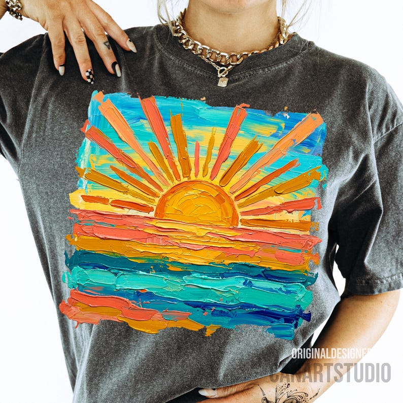 May include: Dark gray t-shirt featuring a vibrant, textured painting of a sunset over the ocean. The artwork uses bold brushstrokes in shades of orange, yellow, blue, and turquoise. The text "ORIGINAL DESIGNER" and "ARTSTUDIO" is visible.