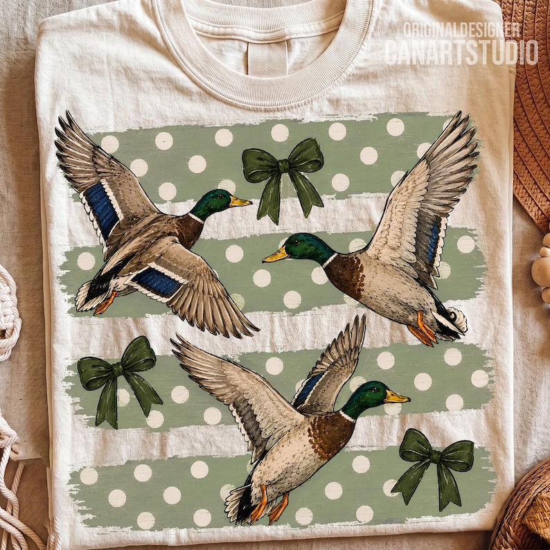 Pu&ograve; includere: Una t-shirt color crema con una stampa grafica di tre germani reali in volo, con teste verdi e macchie alari blu. Il design include tre fiocchi verde scuro e strisce orizzontali verde salvia con pois bianchi sulla parte anteriore.