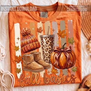 May include: Orange t-shirt with a fall-themed graphic. The design includes a knit hat, boots, a leopard-print tumbler, and a pumpkin with a bow. The words "fall basics" are written in a decorative font. The shirt also has the words "INSTANT DOWNLOAD" and "CANARTSTUDIO".