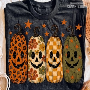 Può includere: Una t-shirt grigio scuro con quattro zucche di Halloween allungate con motivi distinti: leopardato, floreale, a scacchi e stellato. Le zucche hanno volti neri intagliati e sono circondate da piccole stelle arancioni. Testo: CANARTSTUDIO.