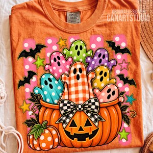 May include: An orange t-shirt featuring a graphic of a large jack-o'-lantern filled with colorful ghosts in polka dot and gingham patterns. The design includes black bats, yellow and green stars, and a black and white checkered bow on the pumpkin.