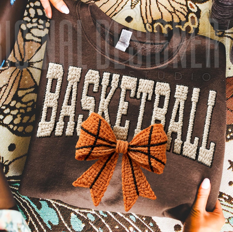 A cozy handmade-style basketball word design with yarn texture and a bow shaped like a basketball. The soft knit details and warm tones create a cozy sporty aesthetic, perfect for basketball-themed crafts and sublimation projects.